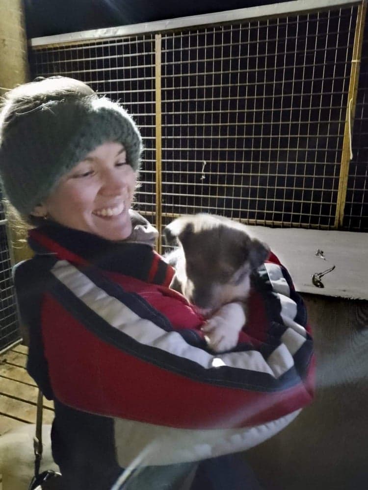 Rebecca wearing the knitted woollen headband while holding a puppy in the Arctic!